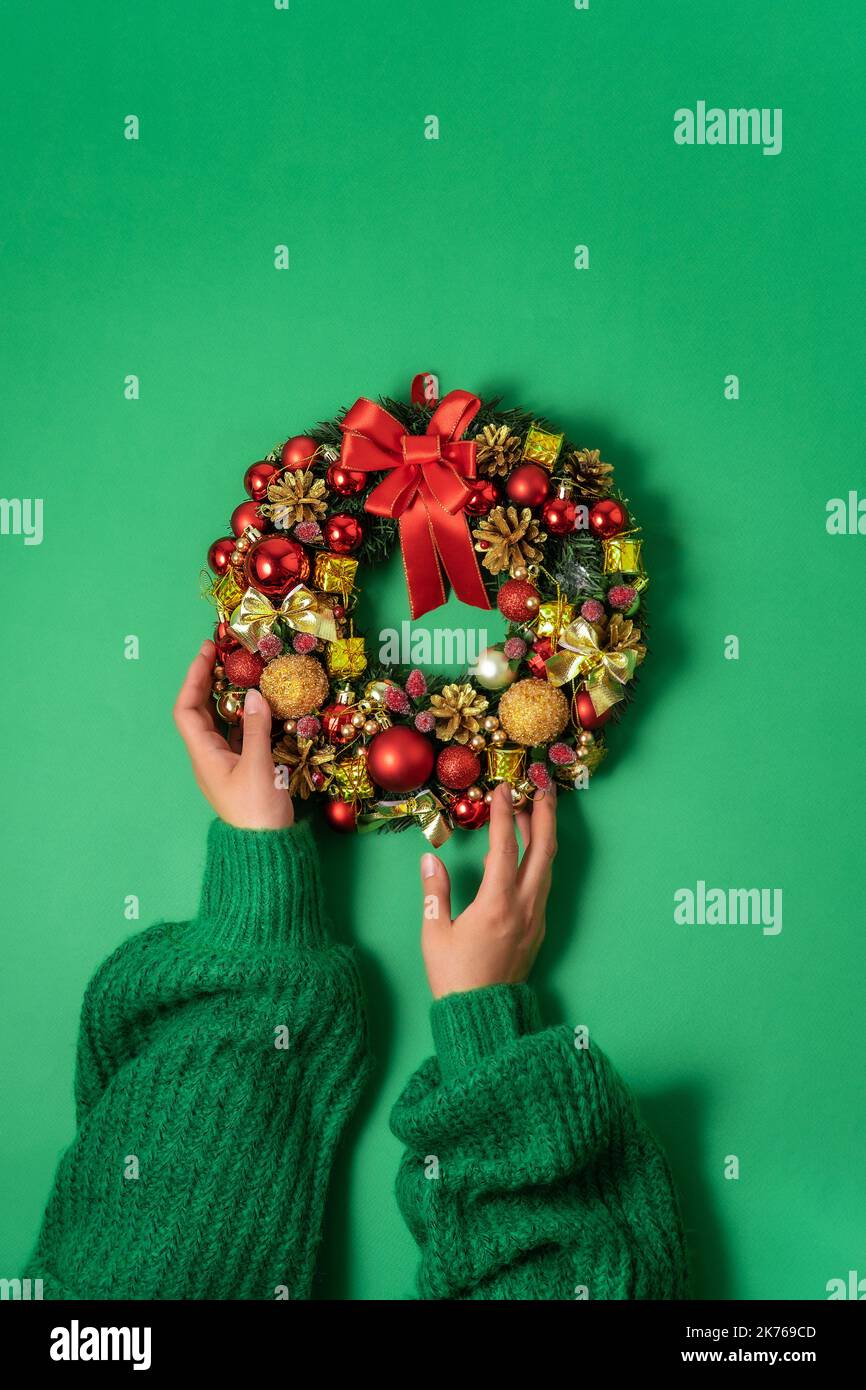 Christmas fir wreath with festive decor in female hands on a green background. Minimalism, the concept of preparation for Christmas and New Year Stock Photo