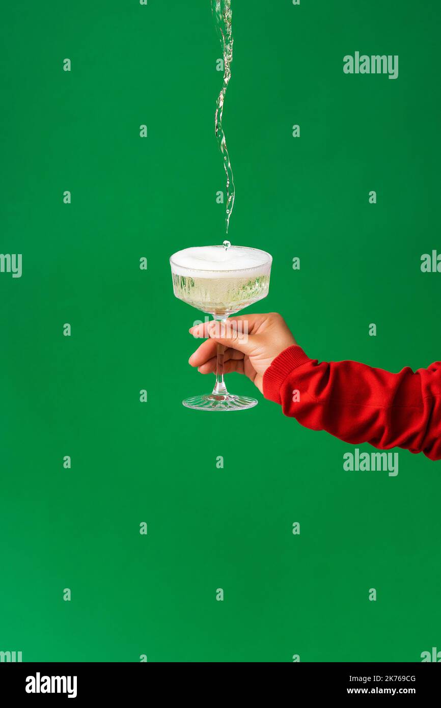 Trendy festive background, a stream of champagne, wine pours from above into a glass in a female hand. Minimalism, the concept of celebrating Christma Stock Photo
