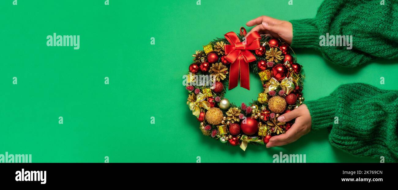 Christmas fir wreath with festive decor in female hands on a green background. Minimalism, the concept of preparation for Christmas and New Year Banne Stock Photo