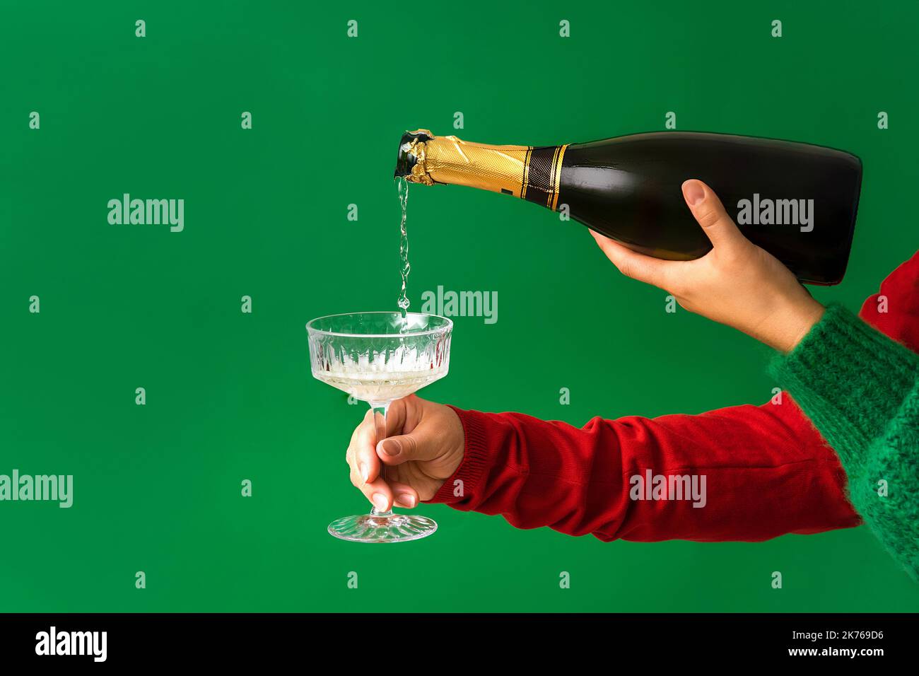 Festive party background, Champagne is pouring from a bottle into a glass in a female hand, green background. Copy space, minimalism, Christmas and Ne Stock Photo