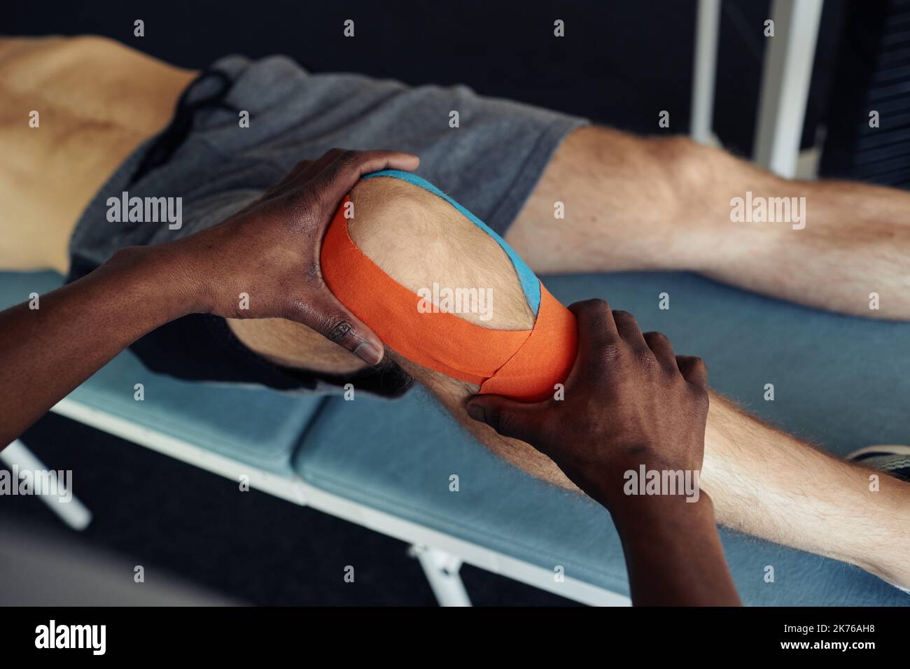 Close-up of therapist applying medical tapes on leg of patient before physical exercises in gym Stock Photo
