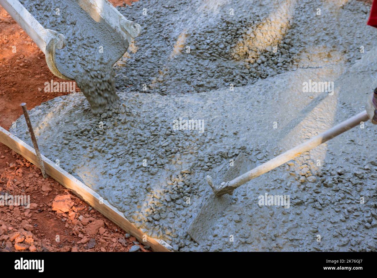 Worker contractor pouring wet concrete while paving driveway by concrete construction Stock