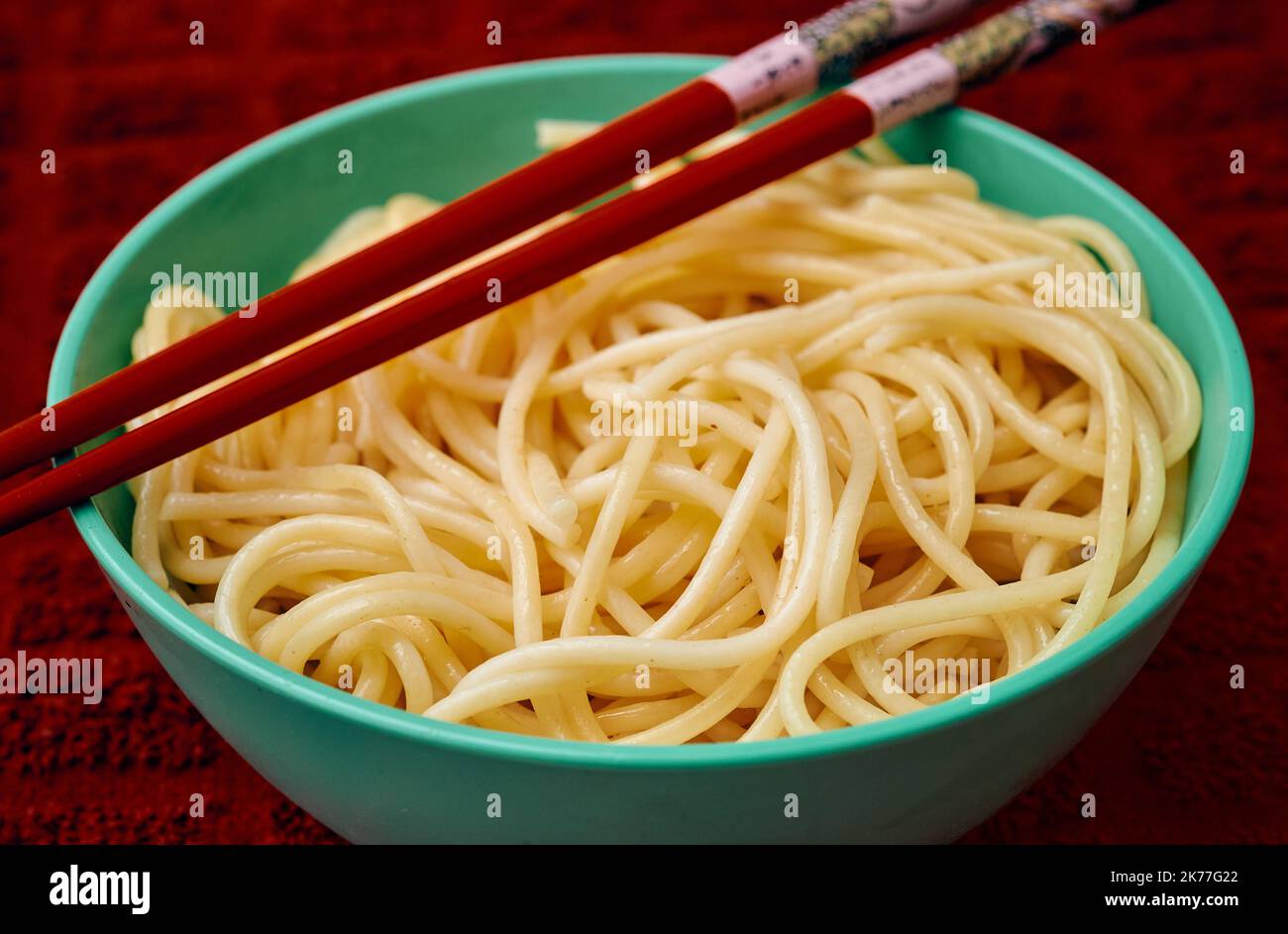 Organic semolina pasta is served in a small teal bowl with red chapstick over a red kitchen towl Stock Photo
