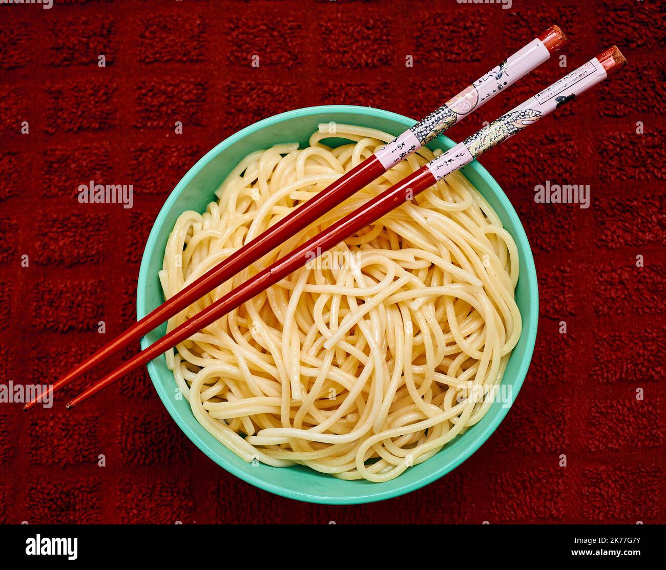 Organic semolina pasta is served in a small teal bowl with red chapstick over a red kitchen towl Stock Photo