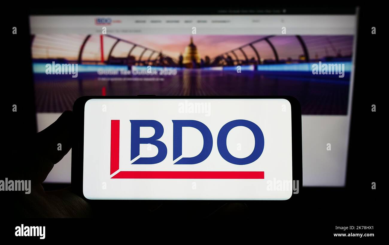 Person holding smartphone with logo of accounting network BDO Global on screen in front of website. Focus on phone display. Stock Photo