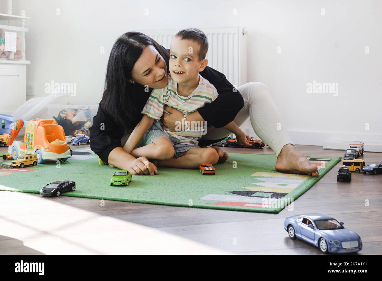 Kid with health problem playing toy cars with mother at home. child having Cerebral palsy entertaining on mat with caregiver Inclusion, rehabilitation Stock Photo