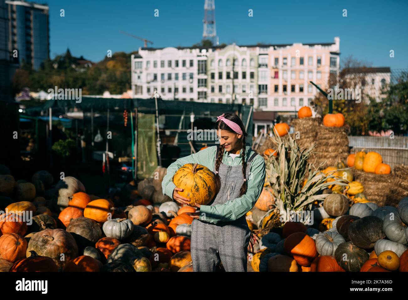 Happy farmer woman in a denim jumpsuit holds ripe pumpkin Stock Photo