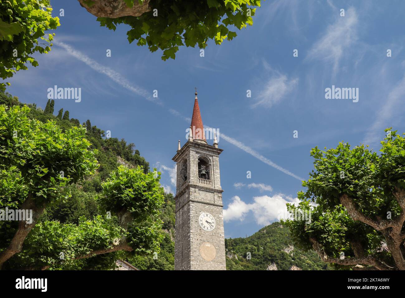 Stone Bell Tower in Varenna. Beautiful Historic Architecture with Green Trees in Province of Lecco during Sunny Day with Blue Sky. Stock Photo