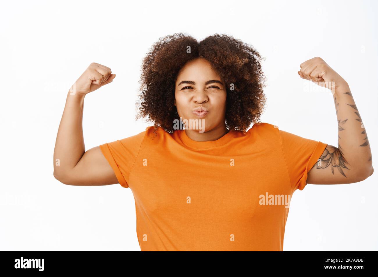Portrait of confident and sassy african american woman, flexing biceps, raising arms and showing her strong muscles, feeling empowered, shouting Stock Photo