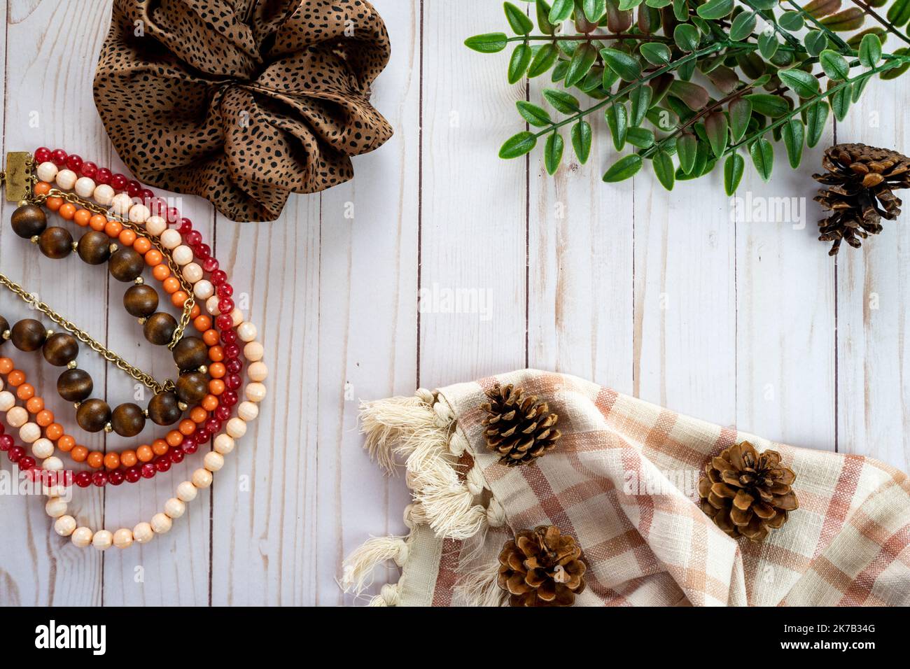 Trendy flat lay top down view with a brown scrunchie, pine cones, plaid towel, green leaves, and a coral pink beaded necklace Stock Photo