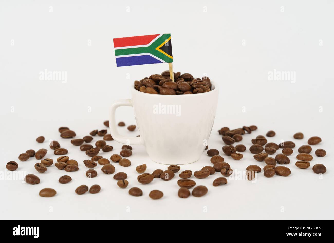 The flag of South Africa sticks out of a cup of roasted coffee beans. Concept of consumption and