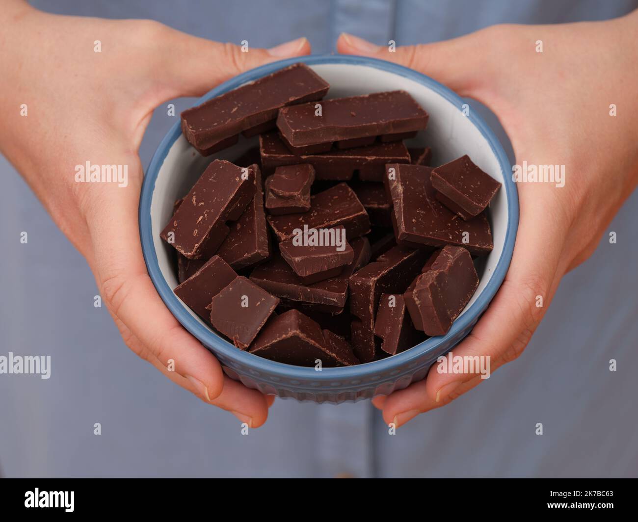 A woman holding a bowl of broken dark chocolate in her hands. Close up. Stock Photo