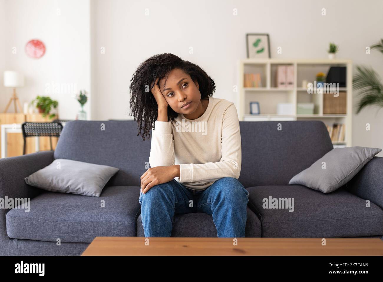 Depressed young adult hispanic latin woman sitting on sofa at home Stock Photo
