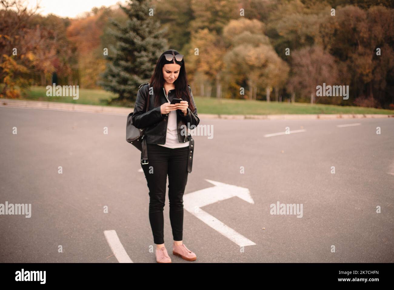 Happy young female traveler using smart phone while standing on the road making choice in what direction to go Stock Photo