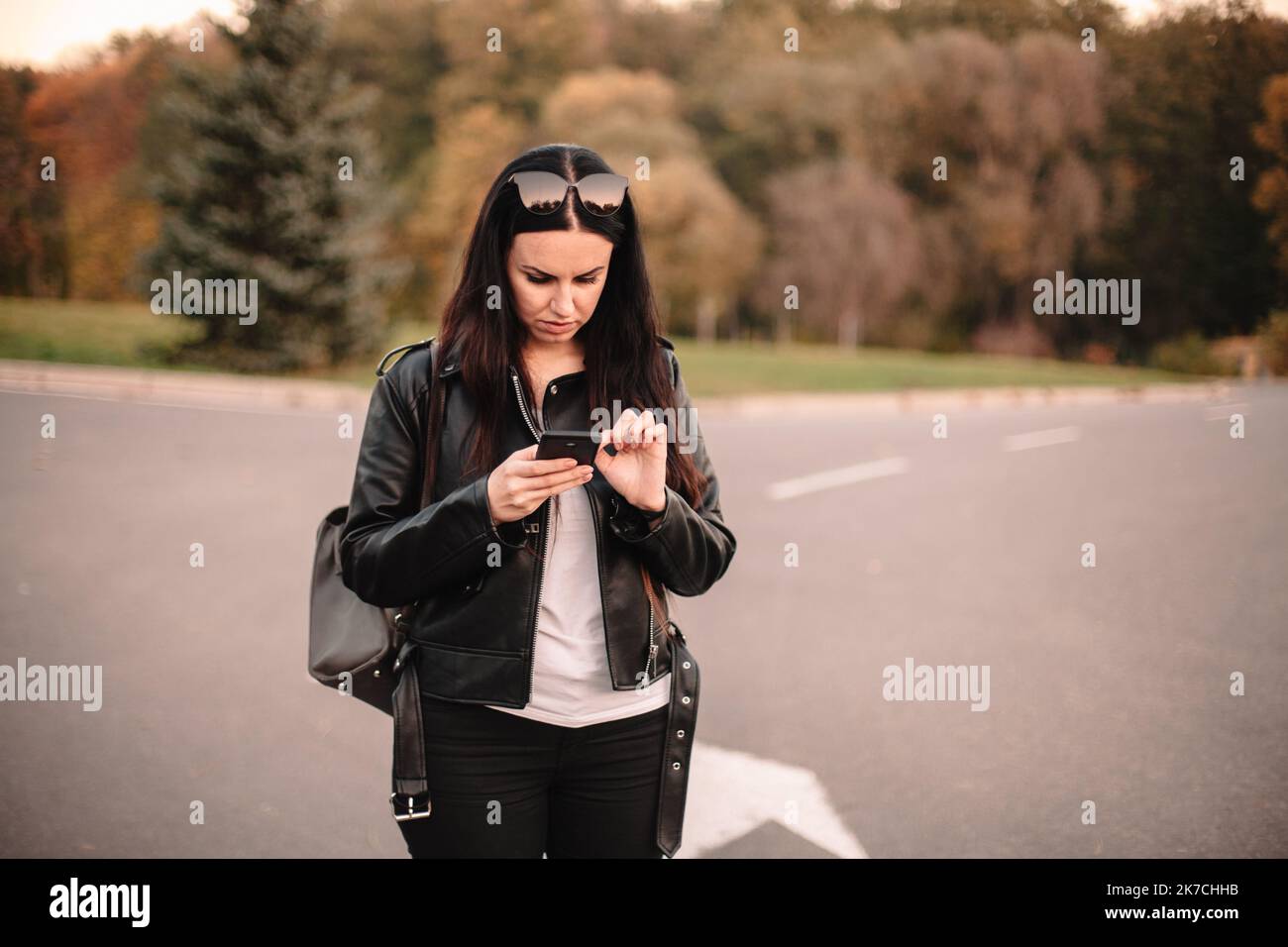 Serious young female traveler using smart phone while standing on the road making choice in what direction to go Stock Photo