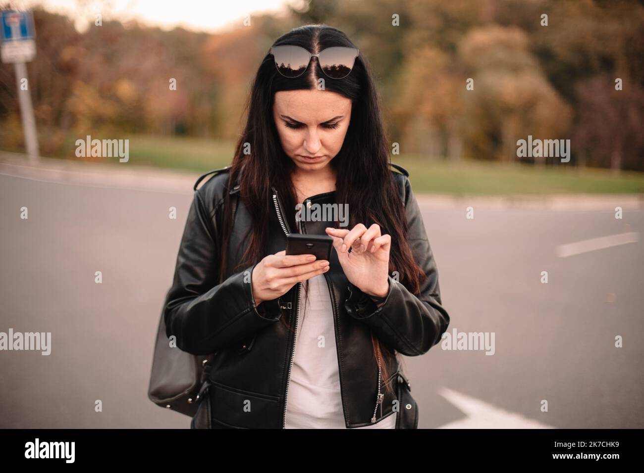 Serious young female traveler using smart phone while standing on the road making choice in what direction to go Stock Photo