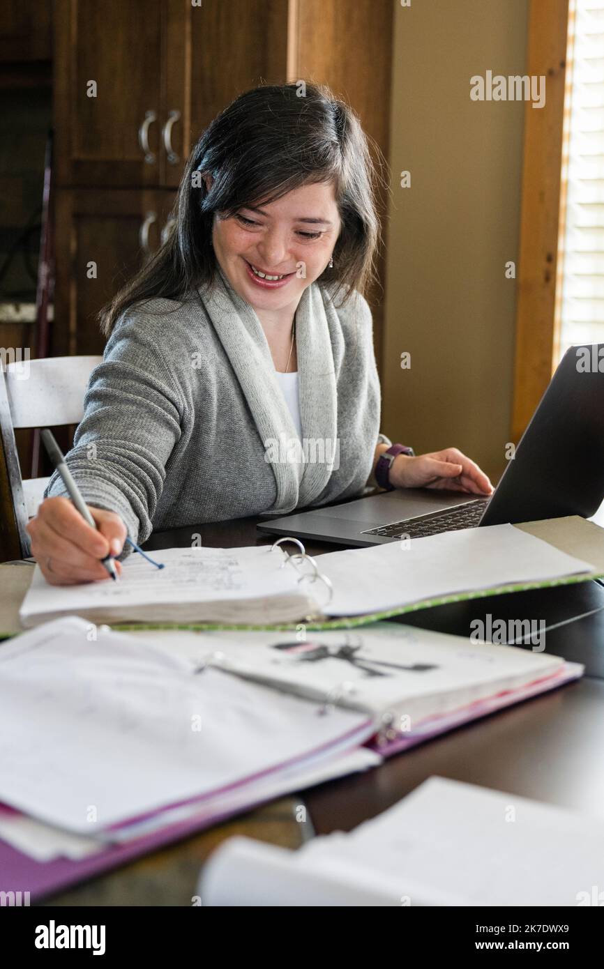 Woman with down syndrome writing notes from laptop at home Stock Photo