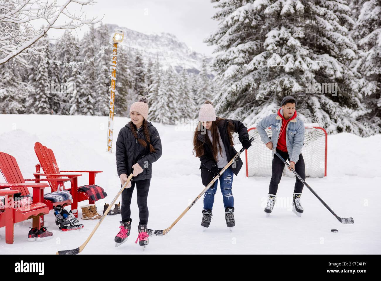 Brother and sisters playing ice hockey at snowy mountain resort Stock