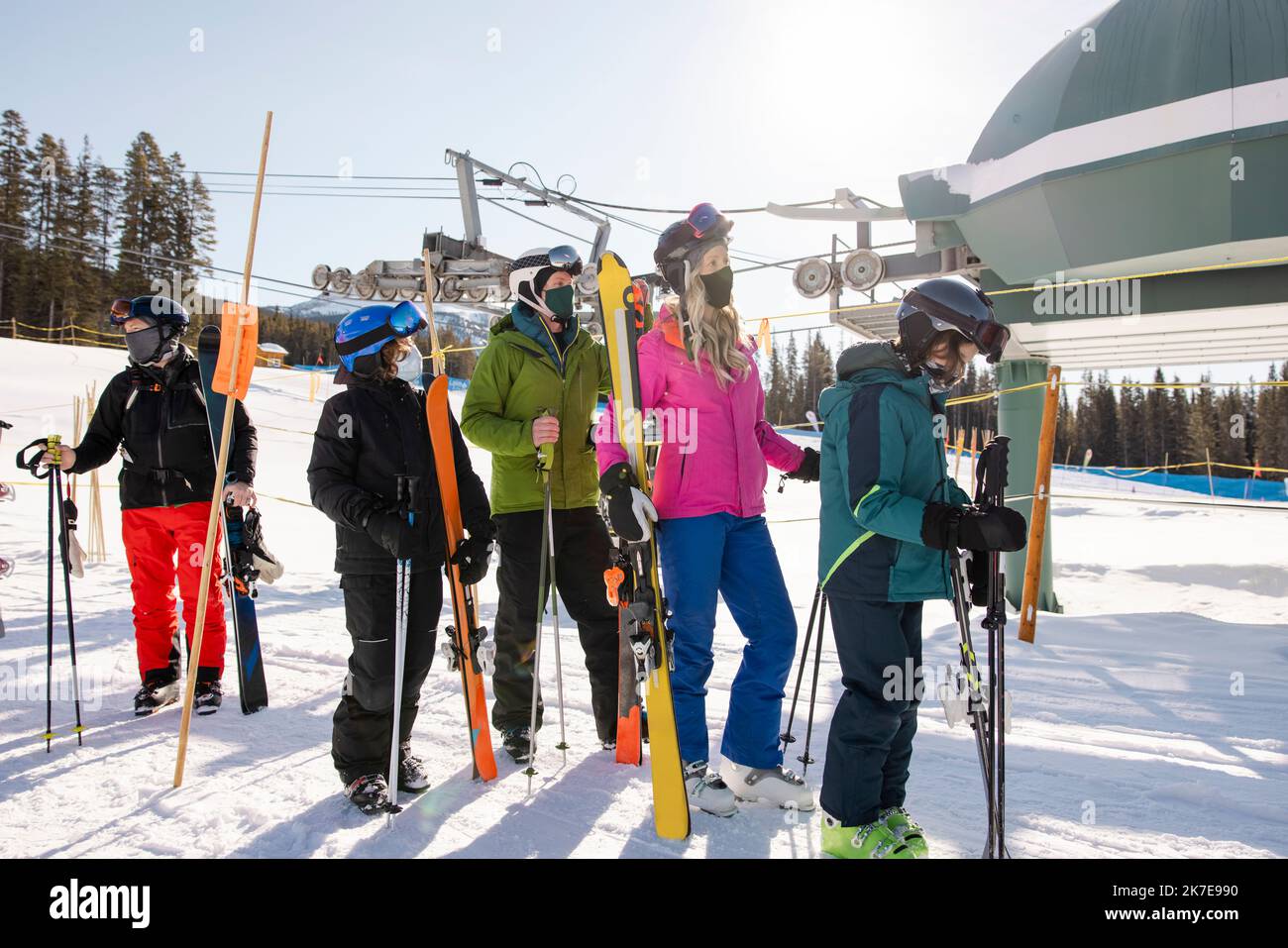 Family with skis in face masks waiting for chair lift at ski resort