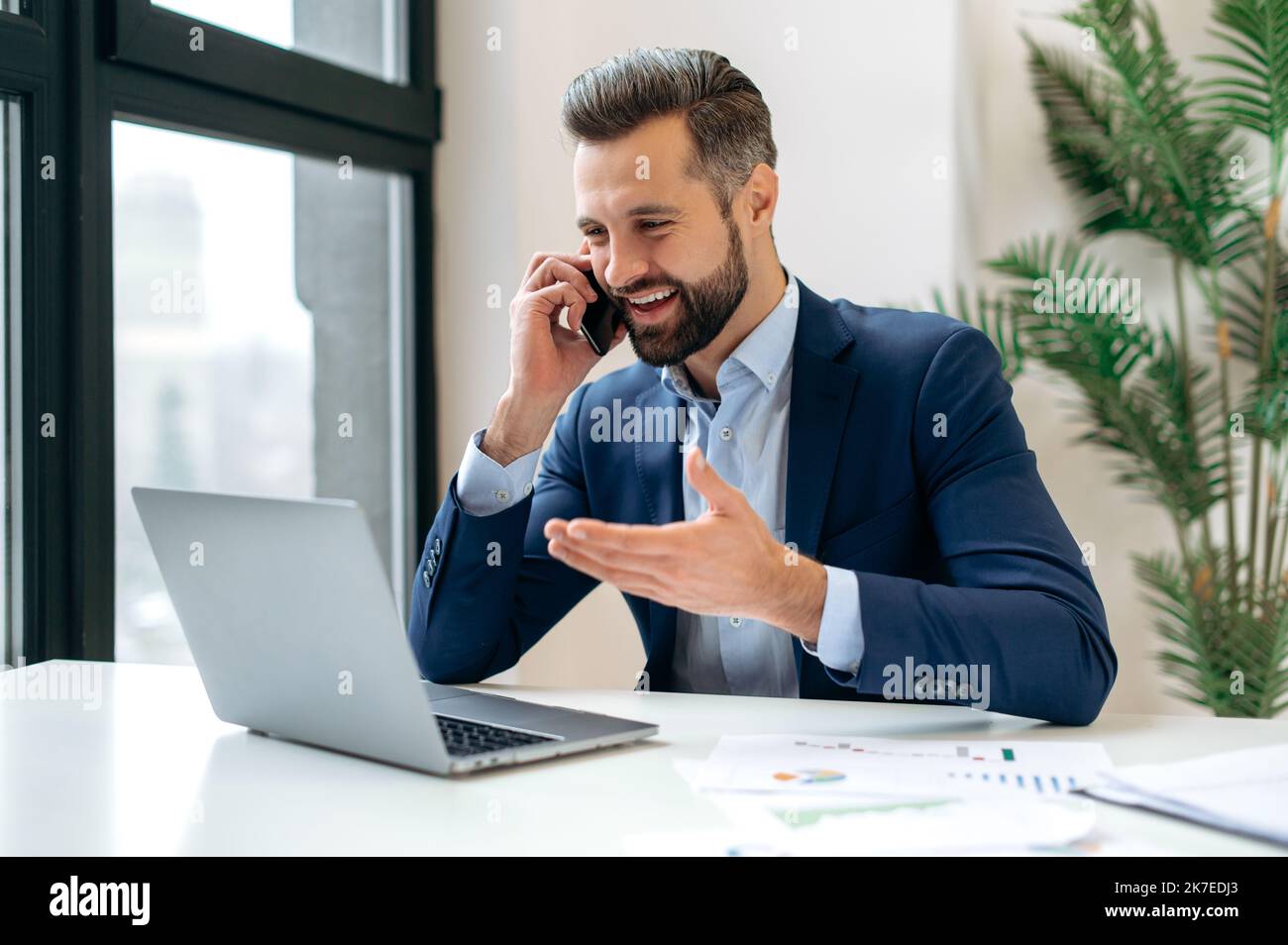 Happy successful busy caucasian man in a suit, company employee, top manager, boss, sitting in the office, talking on the phone with a colleague or client, resolves work issues, smiling Stock Photo