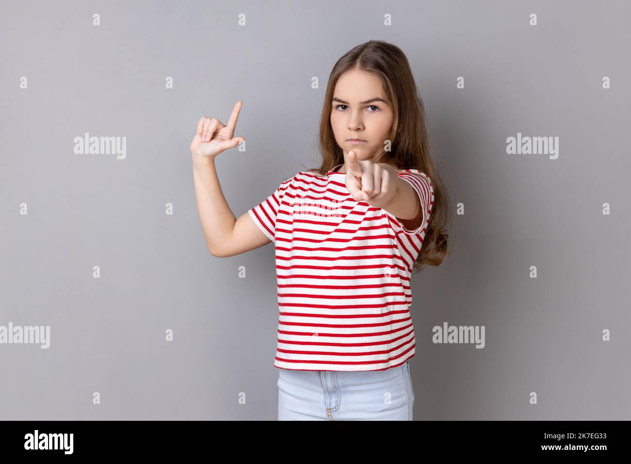 Portrait of serious little girl wearing striped T-shirt showing looser ...