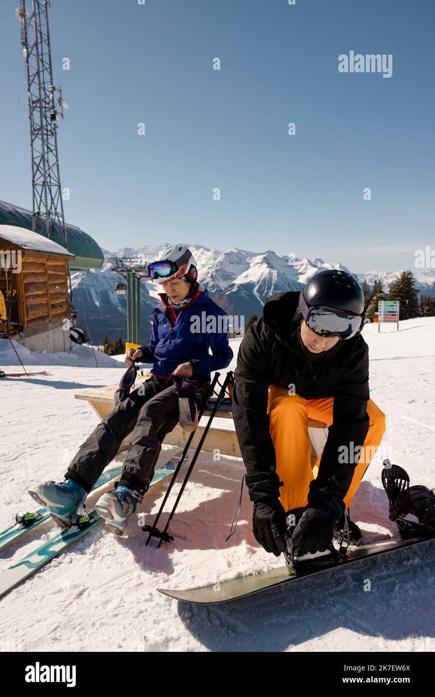 Mother and son preparing skis and snowboard at sunny ski resort Stock