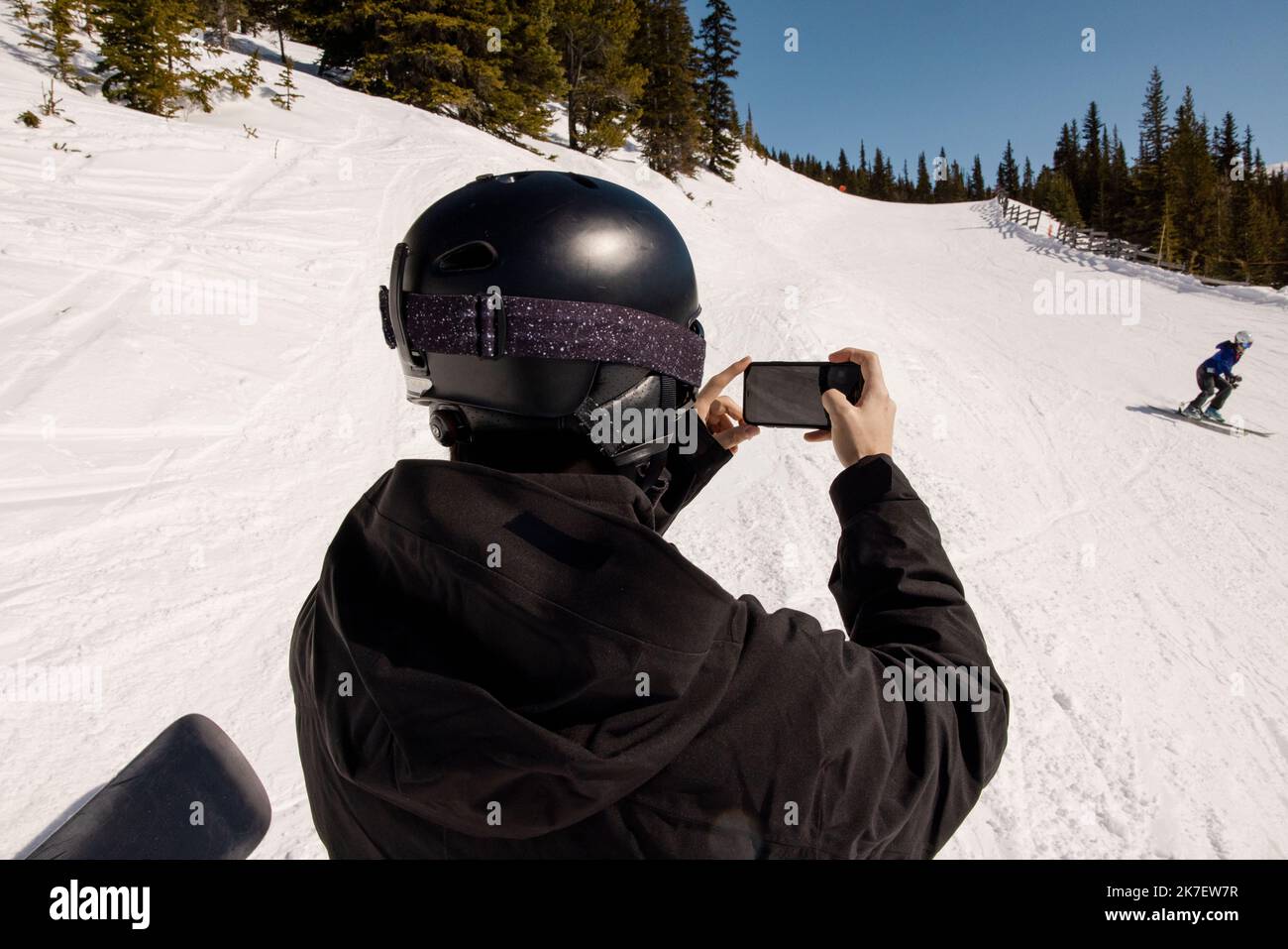 Man with smart phone filming skier on sunny snowy slope Stock Photo