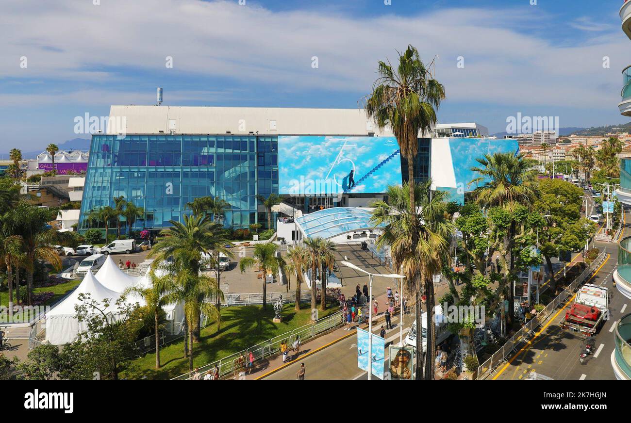 ©PHOTOPQR/NICE MATIN/Patrice Lapoirie ; Cannes ; 16/05/2022 ; Le rituel traditionnel vient d’avoir lieu ce dimanche matin. L’affiche du 75e Festival de Cannes, dont l’image est extraite du film Truman Show, a été hissée et fixée sur le frontispice du Palais. C’est parti pour la Quinzaine du 7è art ! Un homme gravit des marches célestes, qui le mènent vers les nuages, et touche du doigt le '5' de la 75è édition du Festival du film. Allégorie d’un cinéma qui reste synonyme d’évasion et de liberté créatrice, dans un monde où ces valeurs sont parfois menacées? Quoi qu’il en soit, l’affiche du Fes Stock Photo