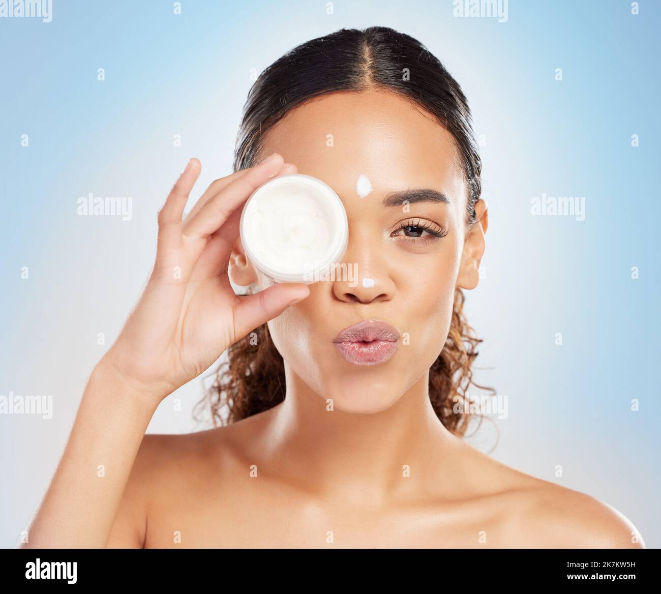 Dont forget to moisturise. a young woman applying cream to her face against a blue background. Stock Photo