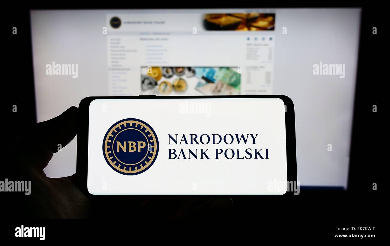 Person holding smartphone with logo of Polish central bank Narodowy Bank Polski (NBP) on screen in front of website. Focus on phone display. Stock Photo