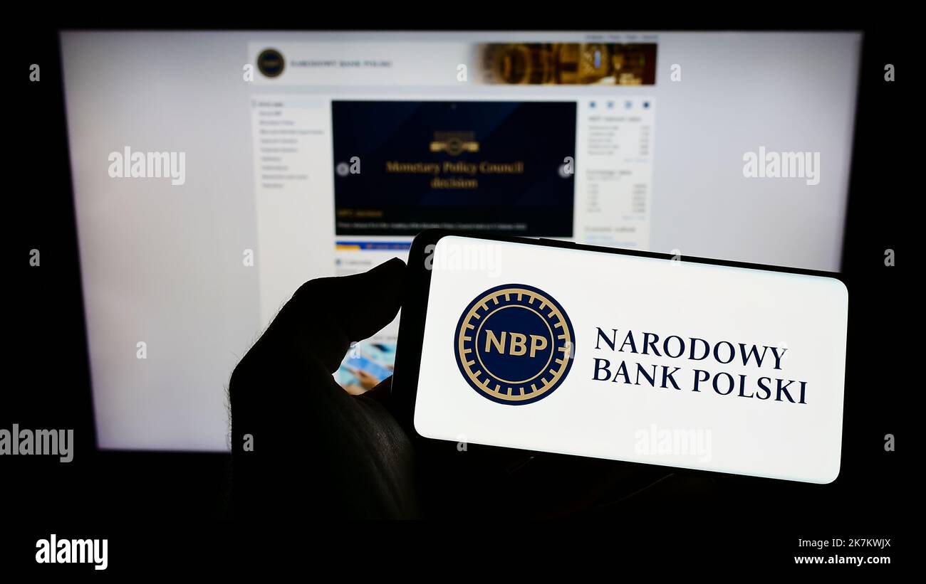 Person holding cellphone with logo of Polish central bank Narodowy Bank Polski (NBP) on screen in front of webpage. Focus on phone display. Stock Photo