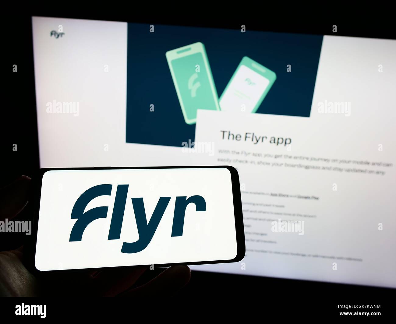 Person holding mobile phone with logo of Norwegian airline company Flyr AS on screen in front of business web page. Focus on phone display. Stock Photo