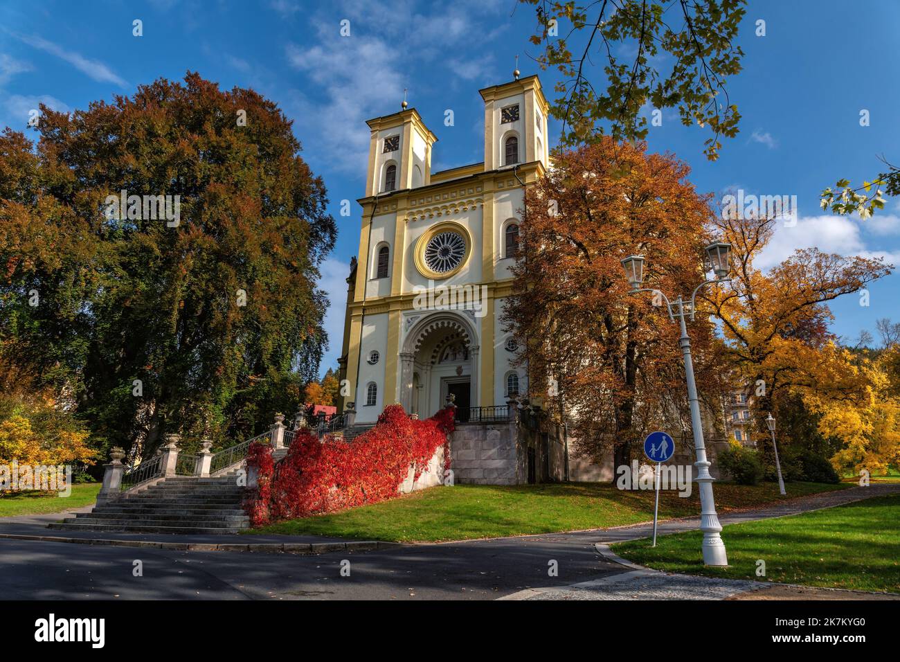 Marianske Lazne (Marienbad) - Catholic Church of the Assumption of the Virgin Mary in the Czech spa town in colorful autumn - blue sky and trees - Stock Image