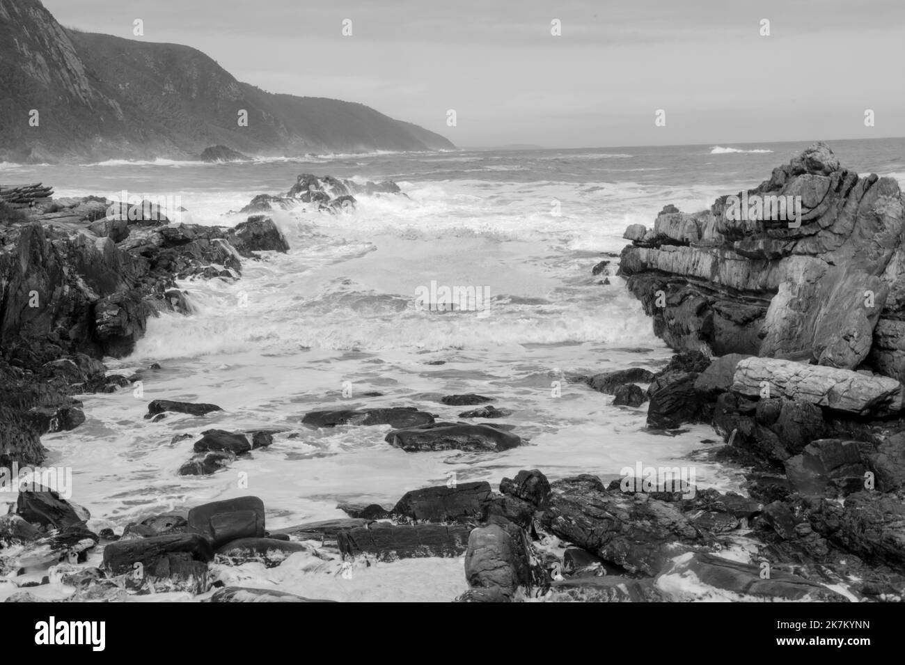 Mono of Storms River seascape creating mood for fine art. Waves Crashing on rocky outcrop spraying fresh sea moist on this scenic destination Stock Photo