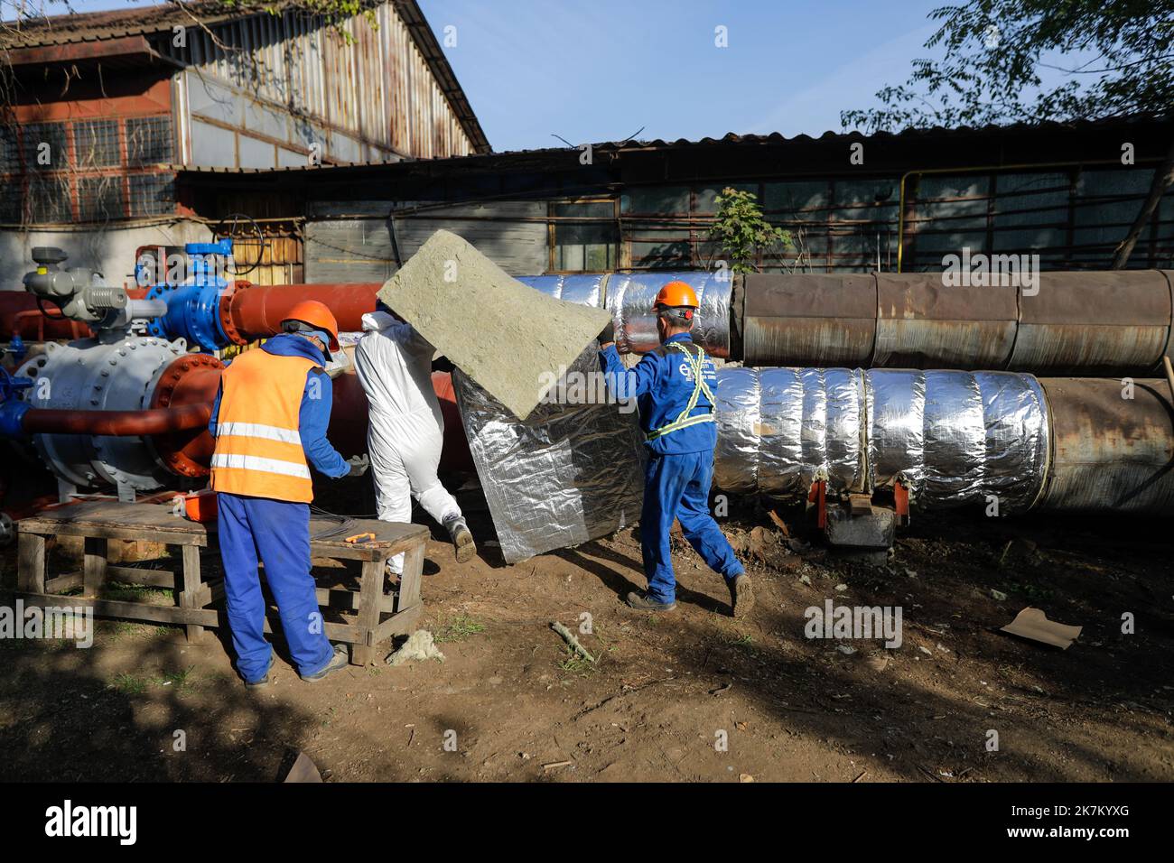 Bucharest, Romania - October 13, 2022: Worker uses glass wool to thermal insulate a hot water metallic pipeline. Stock Photo