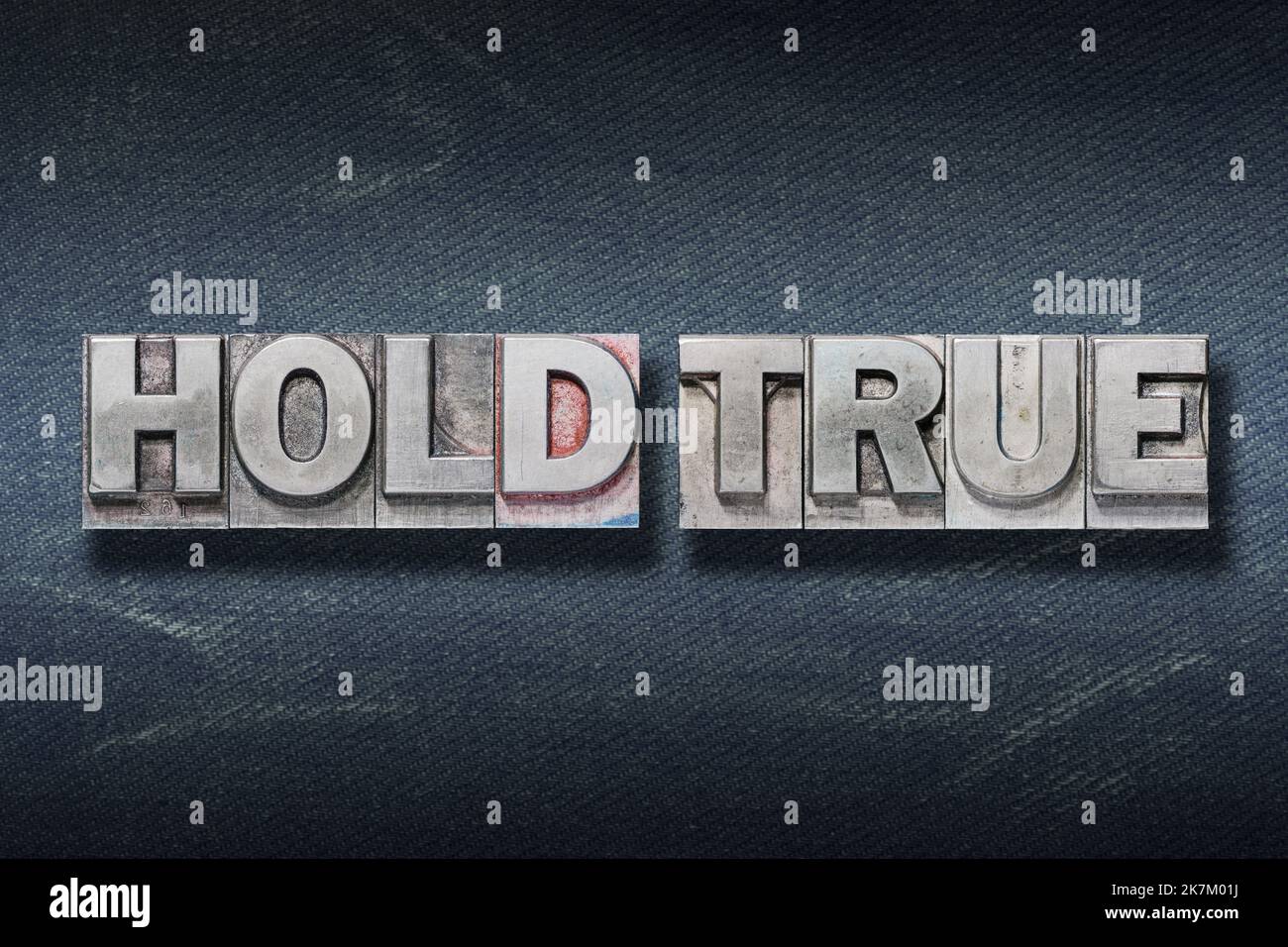 hold true phrase made from metallic letterpress on dark jeans background Stock Photo