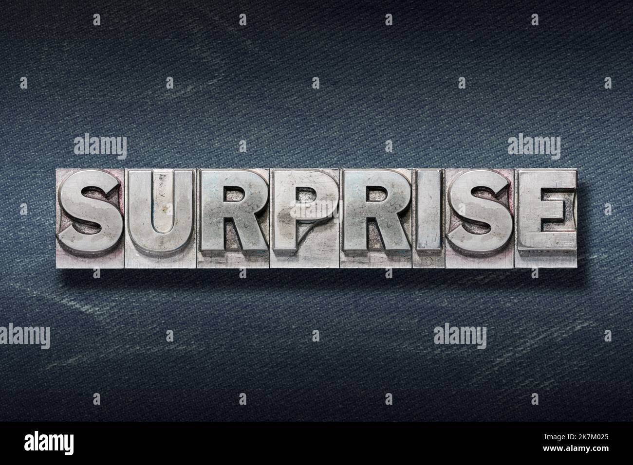 surprise word made from metallic letterpress on dark jeans background Stock Photo