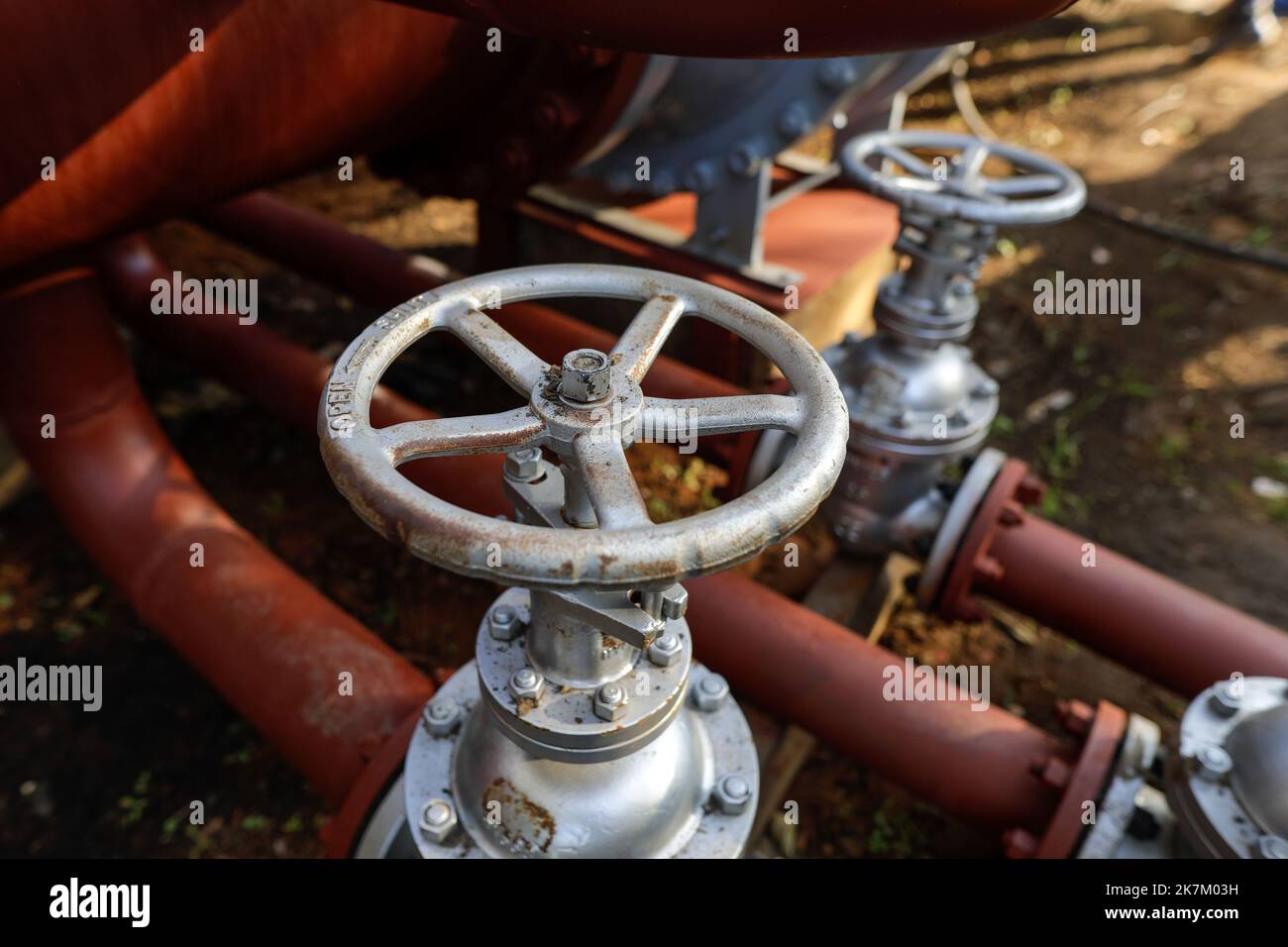 Shallow depth of field (selective focus) details with industrial metallic pipe valves used to open or close the hot water debit inside a big pipeline. Stock Photo