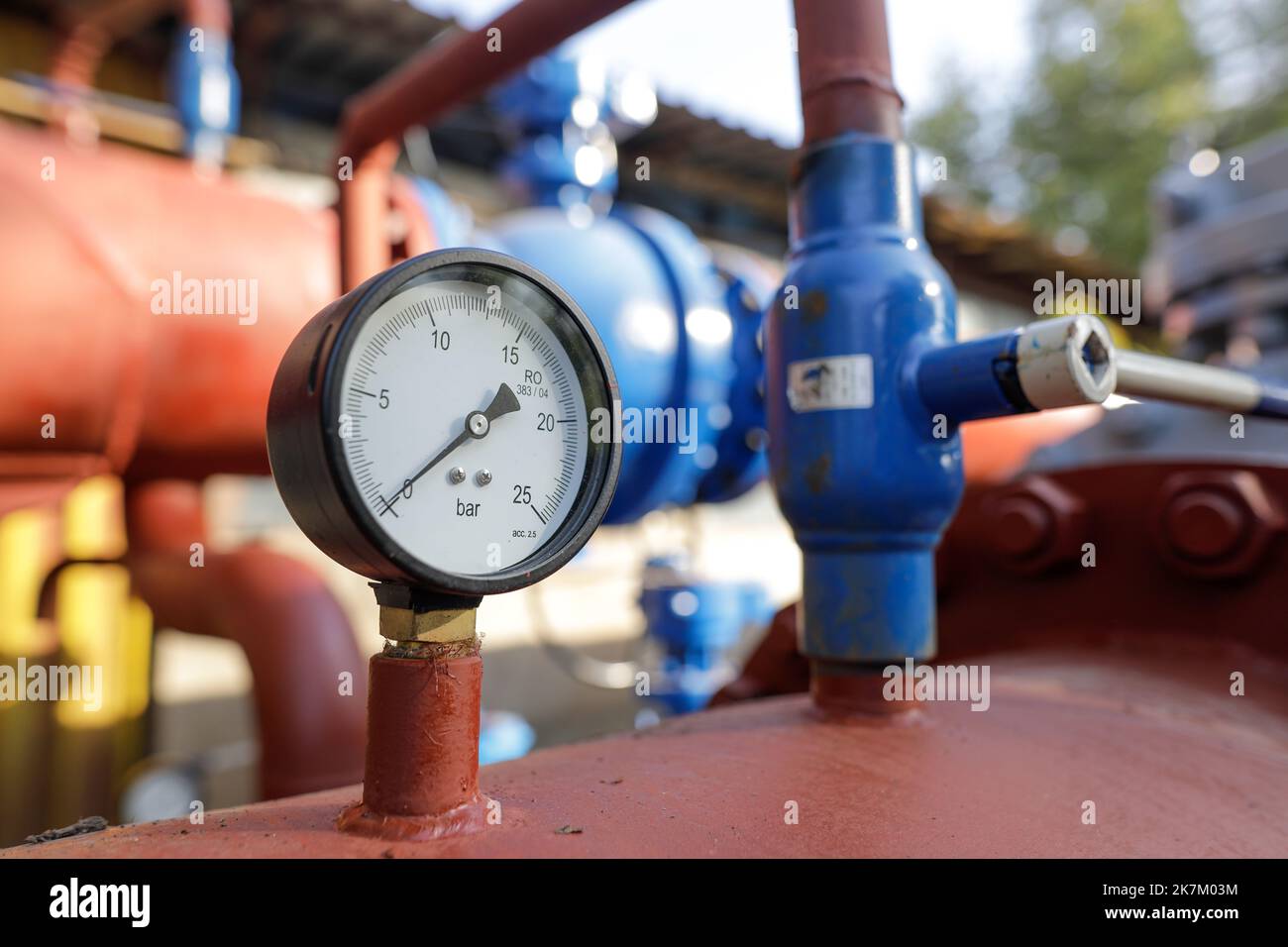 Shallow depth of field (selective focus) details with industrial pressure gauge on an industrial metallic hot water pipeline. Stock Photo