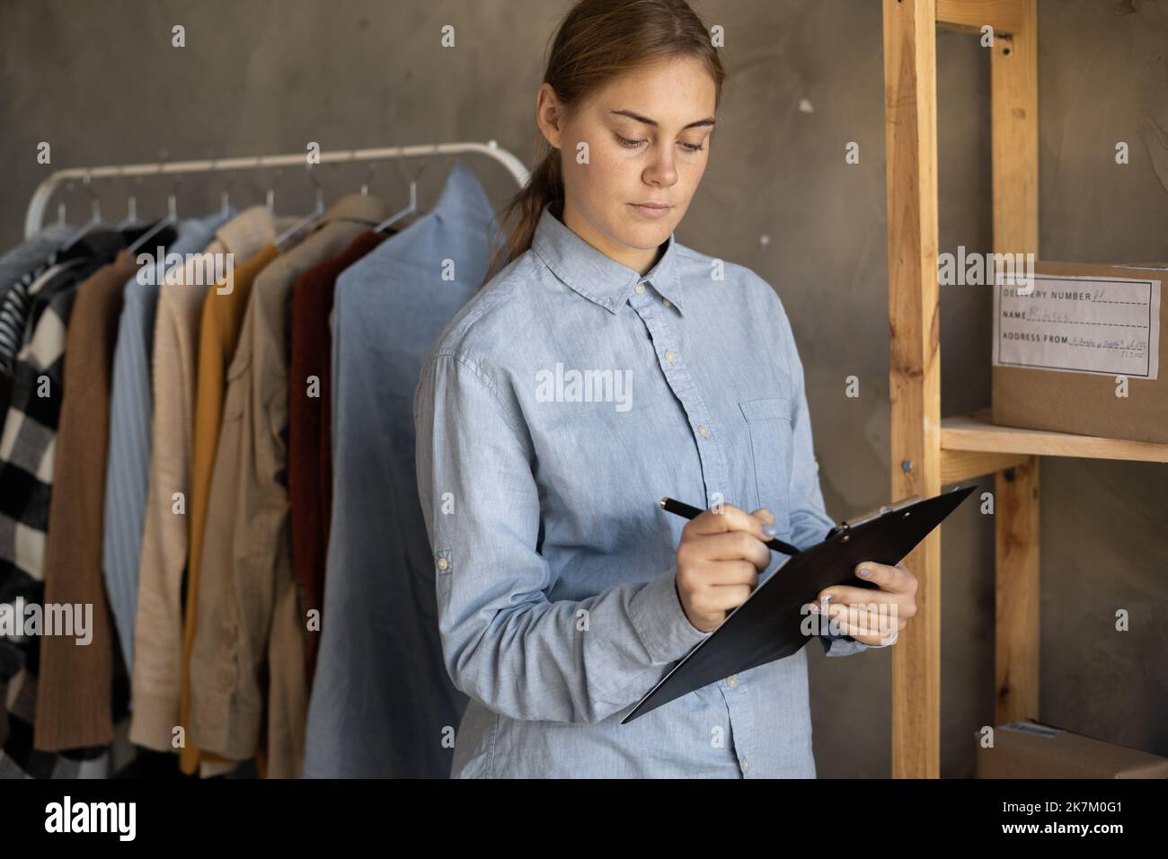 Female small business owner, entrepreneur, shipment delivery dropshipping service worker checking ecommerce order standing in warehouse with clipboard Stock Photo