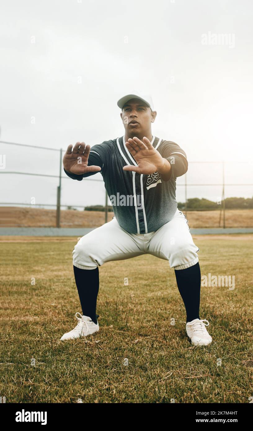 Baseball player, stretching and sports man doing squats on field for warm up exercise, workout and practice for match. Male athlete with tshirt and Stock Photo