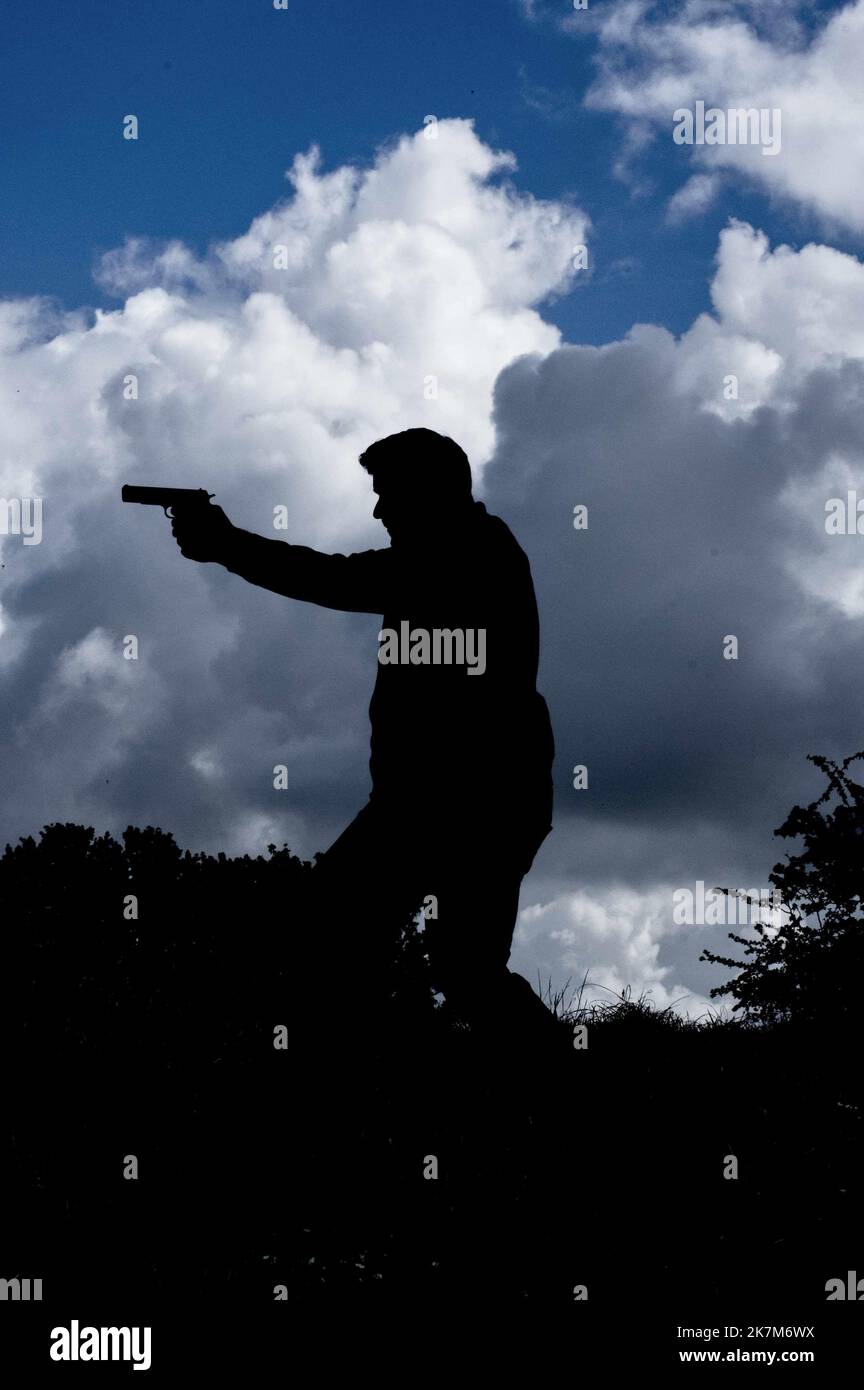 Silhouette of man with gun against a cloudy sky book cover style. Stock Photo