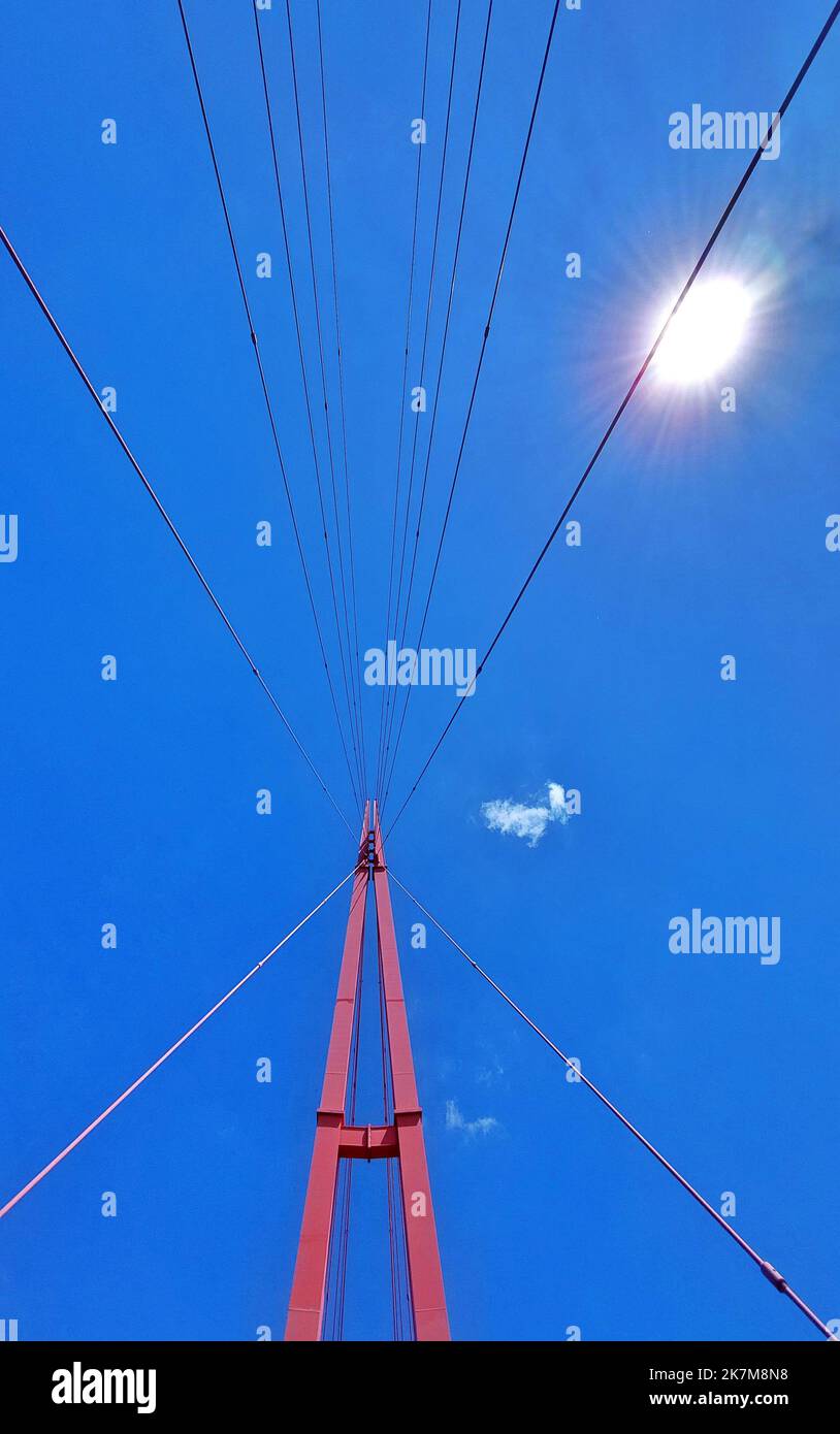 Upward shot from modern suspension bridge with sun and blue sky. Stock Photo