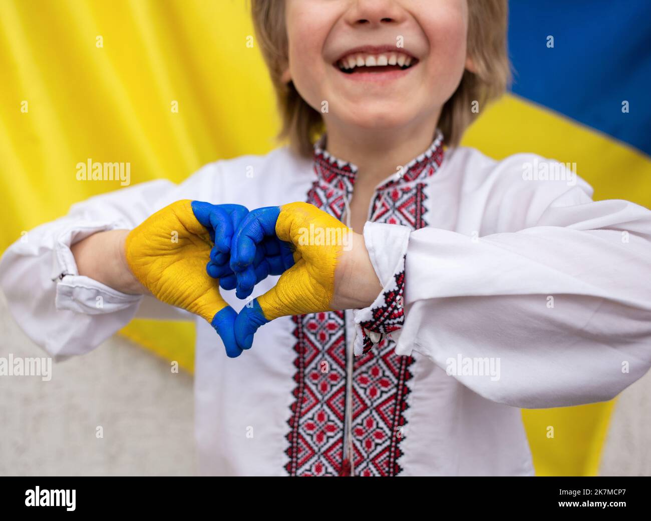 unrecognizable joyful child against background of Ukrainian flag with hands folded in shape of heart, painted in yellow and blue. Children against war Stock Photo