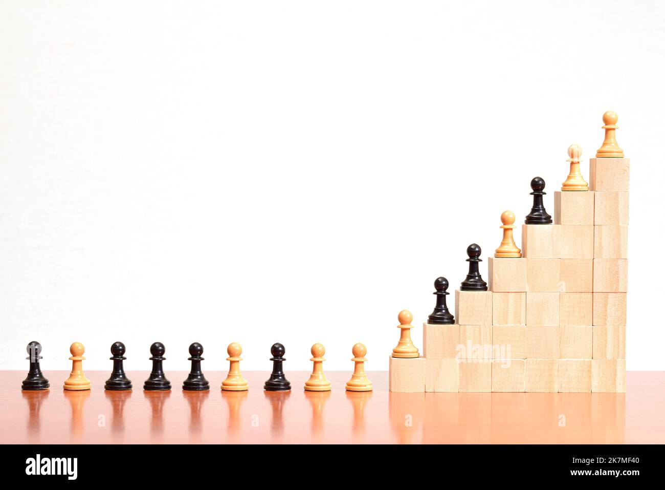 Black and white chess pawns lined up on a staircase made of wooden blocks, with a white background. Concept of growth, improvement, leadership, and su Stock Photo