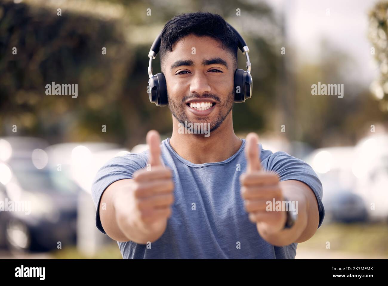 I just heard the song of the century. a young man using headphones and showing thumbs up while standing outside at college. Stock Photo