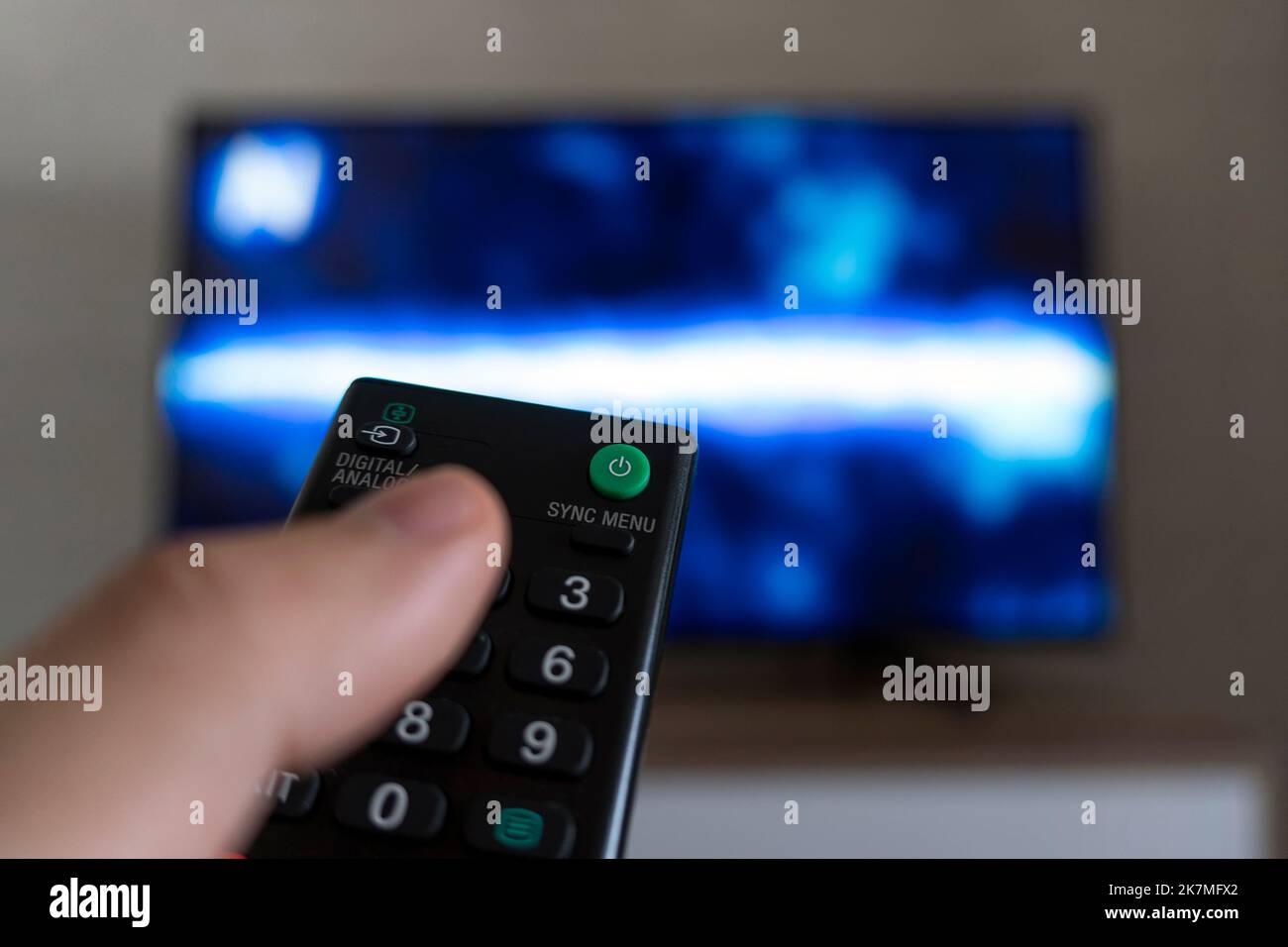 The man with the remote control in hand watching the sports channel and presses the button on the remote control. Remote control in hand closeup. Stock Photo