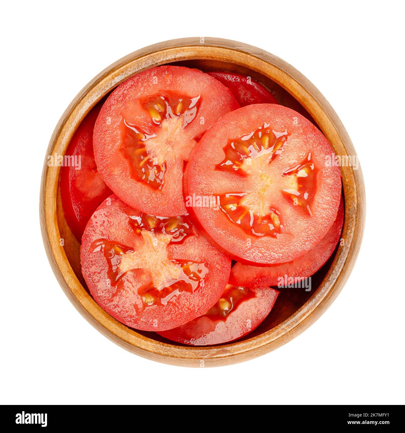Fresh plum tomato slices, in a wooden bowl, isolated from above. Sliced red ripe oval tomatoes, layered on top of each other. Stock Photo