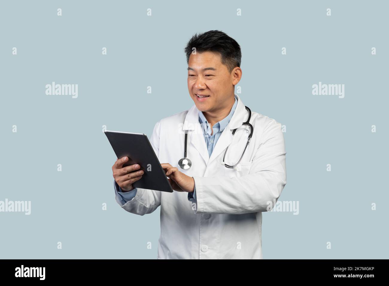Cheerful middle aged chinese male therapist in white coat typing on
