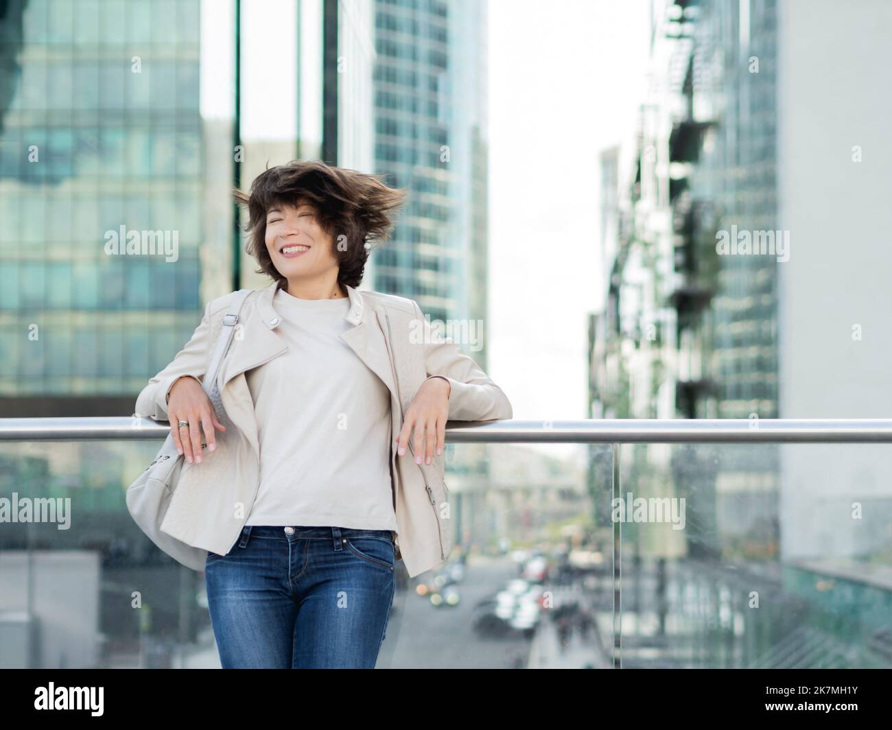 Smiling woman with ruffled hair on background of modern buildings. Downtown with skyscrapers and finance business centers. Urban lifestyle Stock Photo